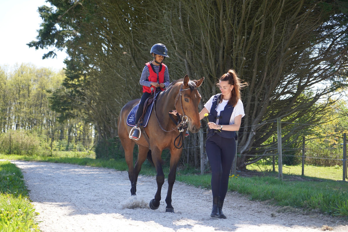 Jeune cavalière à cheval accompagnée d'une femme portant un gilet airbag Hit-Air